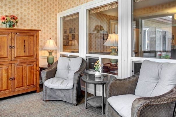 Lounge area with two chairs, a small table, and a cabinet in a senior living facility.