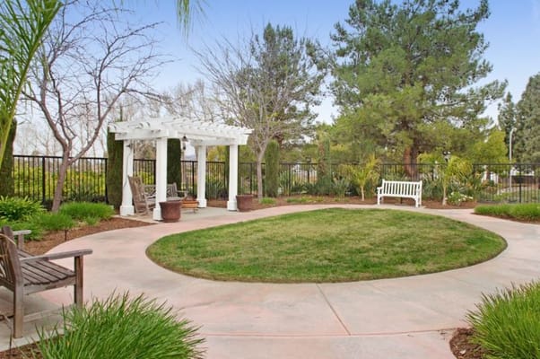 A tranquil garden area with a pergola and benches surrounded by greenery.