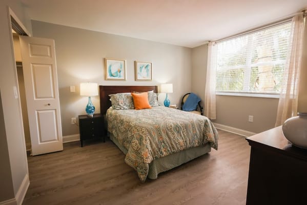 A cozy bedroom with a bed, decorative pillows, and natural light from a window.