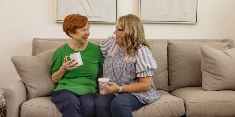 Two women enjoying coffee on a sofa in a cozy common area