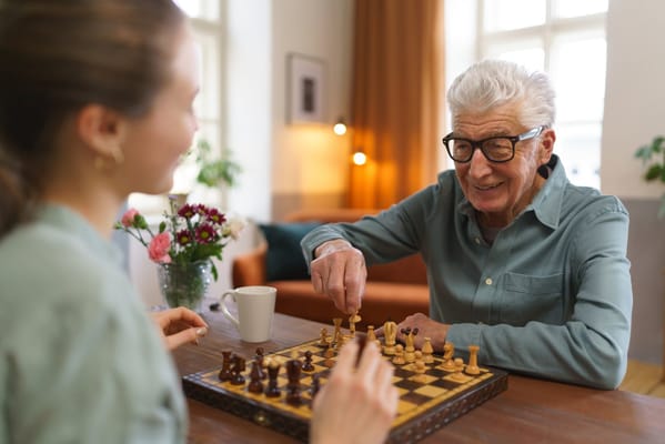 An elderly man playing chess with a caregiver