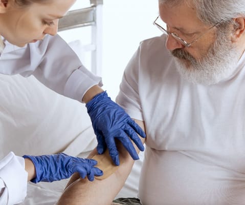 Nurse caring for a senior man's arm in a private room