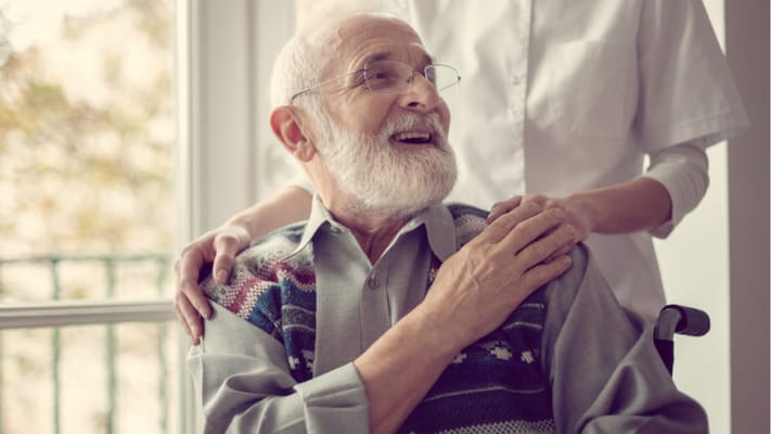 Caregiver assisting a smiling elderly man at a facility