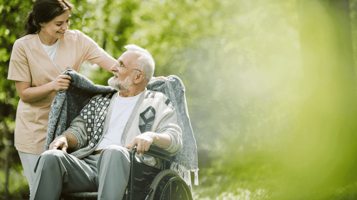A caregiver assisting a senior in a wheel chair outdoors