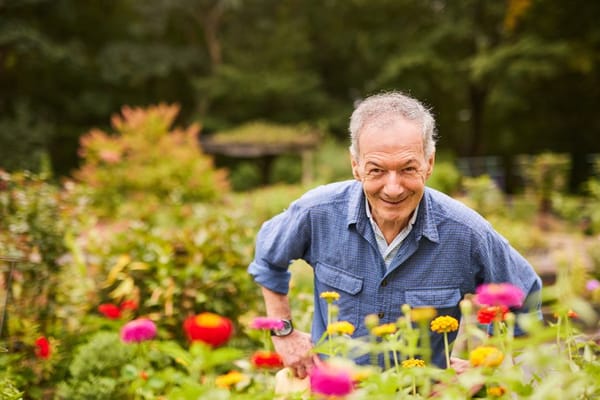 Senior man smiling in vibrant garden full of flowers