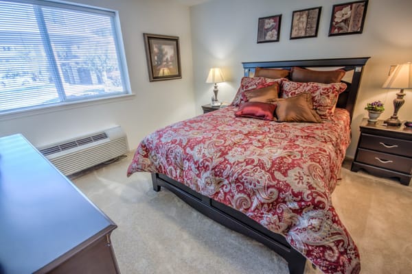 A stylish bedroom with a large bed adorned with a colorful bedspread, lamps on bedside tables, and window light.