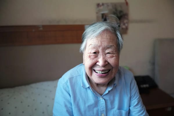 An elderly woman smiling warmly in her room