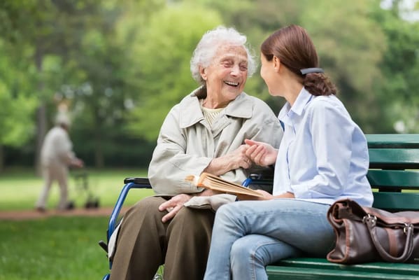 A senior woman laughing with a caregiver on a bench