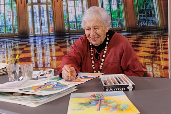 An elderly woman painting in a well-lit activity room