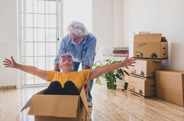 Happy seniors playing in a moving box indoors