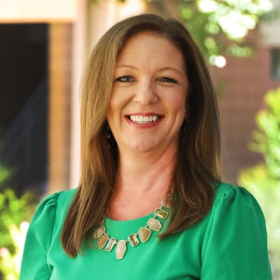 A smiling woman in a green top with a necklace