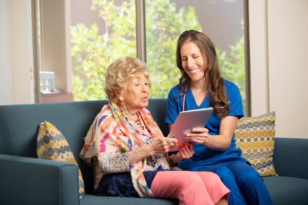 A resident and staff member engaging with a tablet on a sofa