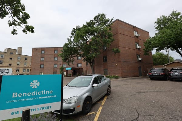 Exterior of Benedictine Living Community building with sign and parked cars