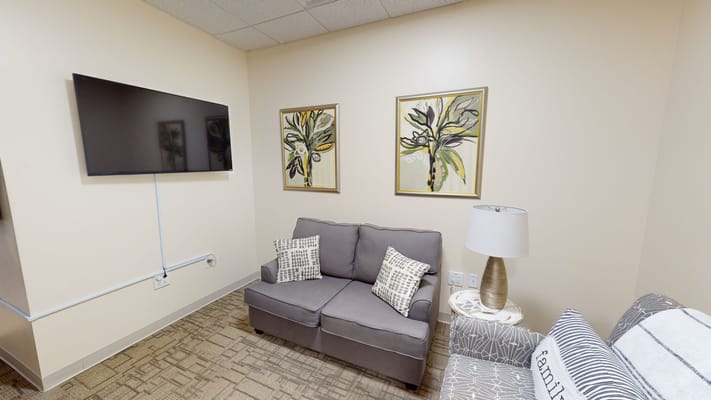 Lounge area with a gray sofa, decorative pillows, lamp, and artwork on the walls.