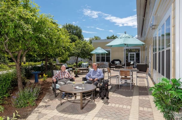 Two elderly men enjoying drinks on a patio with a dog.