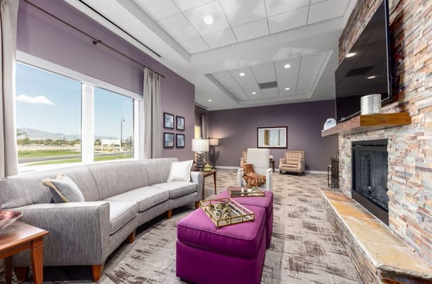 Lounge area with a gray sofa, purple ottoman, and fireplace