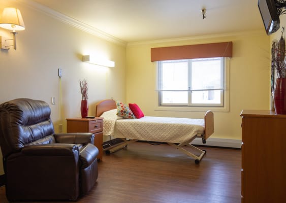 A well-furnished bedroom with a bed, recliner chair, and bedside table.
