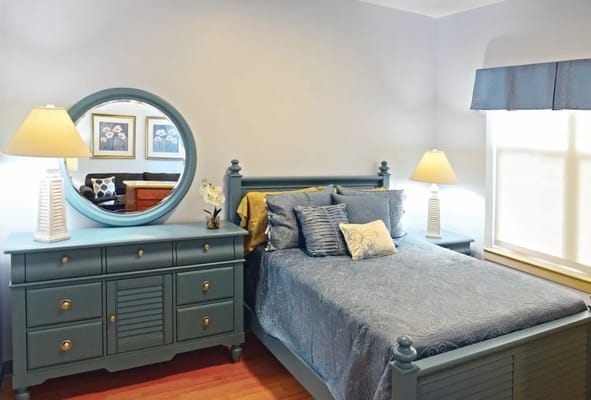 A well-decorated bedroom featuring a bed, dresser, and lamp.