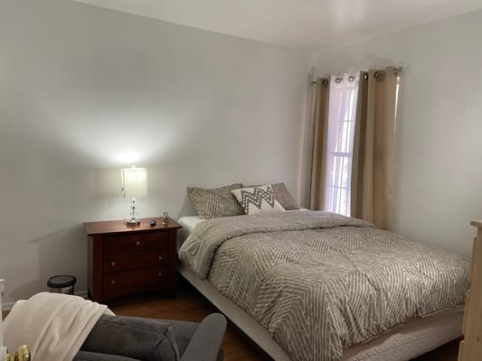 A well-furnished bedroom with a bed, nightstand, and curtains