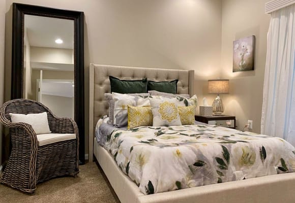 A well-decorated bedroom featuring a bed with floral bedding, a mirror, and a wicker chair.