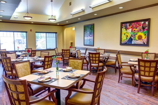 A bright dining room with tables set for meals in Mt. Bachelor Assisted Living