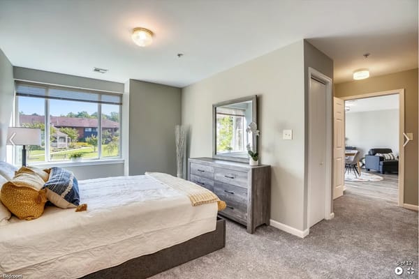 Bright bedroom featuring a bed, dresser, and large window with outdoor view.