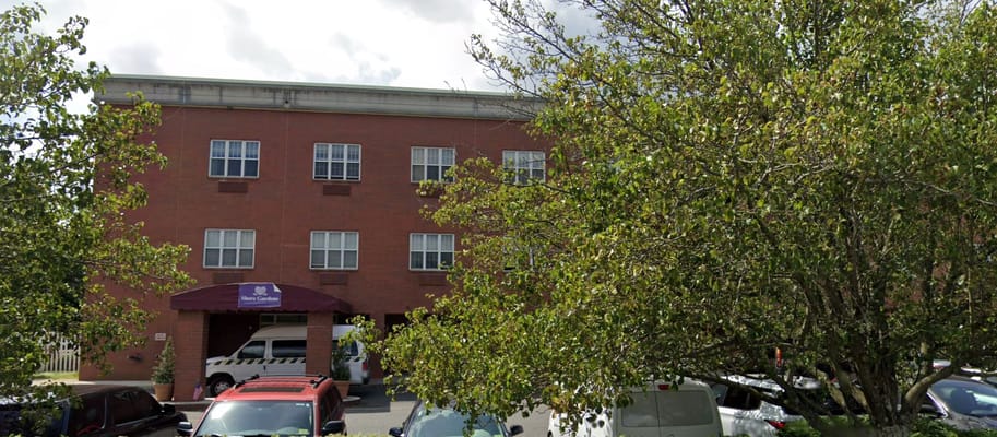 Front view of Shore Gardens Rehabilitation & Nursing Center with trees and parking area