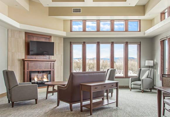 Comfortable lounge area with seating and a fireplace in a senior living facility.
