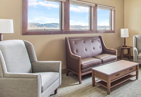 Cozy lounge area with a brown sofa, gray armchair, and coffee table near large windows