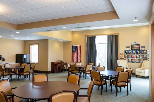 Interior view of the common room with tables and chairs, American flag, and framed photographs.