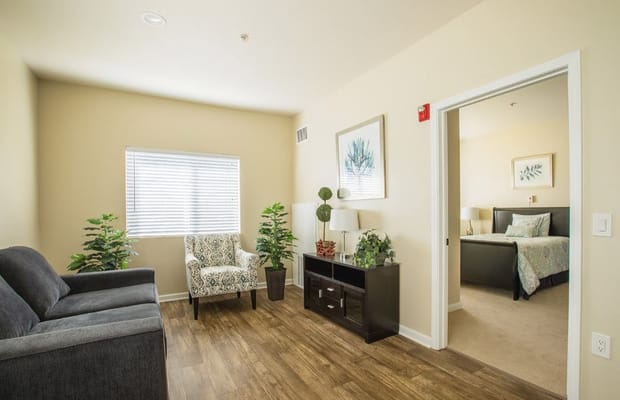 Living room with a couch and plants, leading to a bedroom