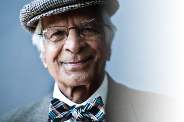 A smiling elderly man wearing a bow tie and cap