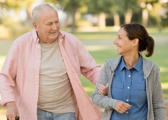 A senior man and a caregiver walking in a sunny outdoor space
