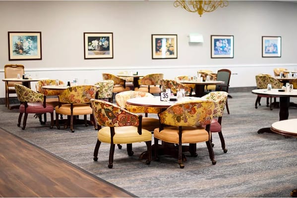 A dining room with floral patterned chairs and tables set for meals.