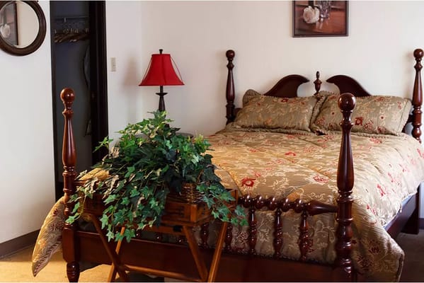 A cozy bedroom featuring a decorative wooden bed, a bedside lamp, and potted greenery.