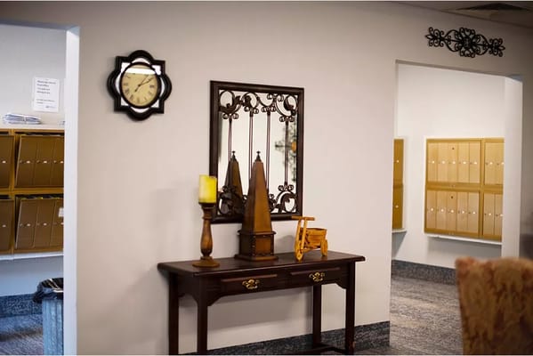 A lobby area with a clock, a mirror, and decorative items on a table.