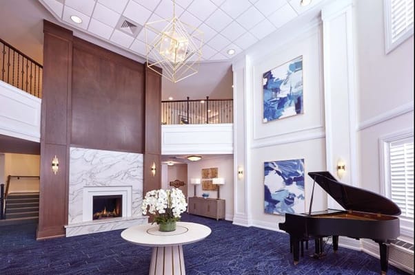 Bright and airy lobby with a piano, fireplace, and decorative paintings