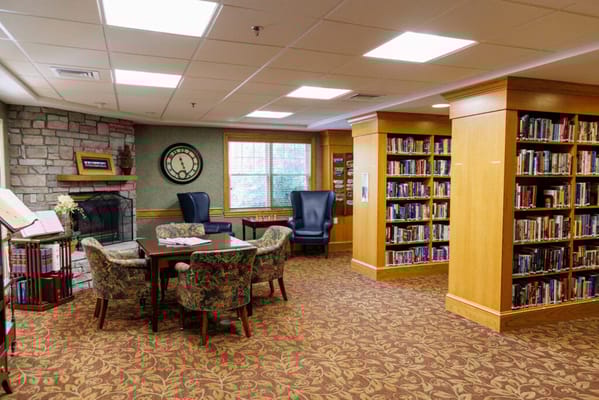 Cozy library with bookshelves, seating areas, and a fireplace.