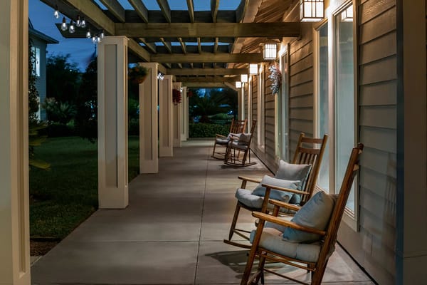 Rocking chairs on a porch with overhead lights at twilight