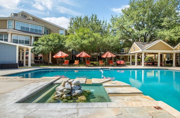Outdoor pool with a stone fountain and lounge chairs under umbrellas