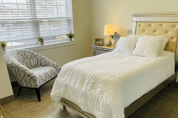 Bright bedroom with a bed, a chair, and a lamp.