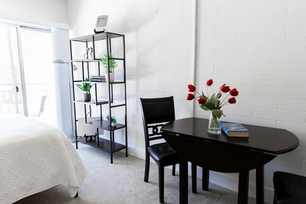 Spacious bedroom with a table, chair, and shelf decorated with plants
