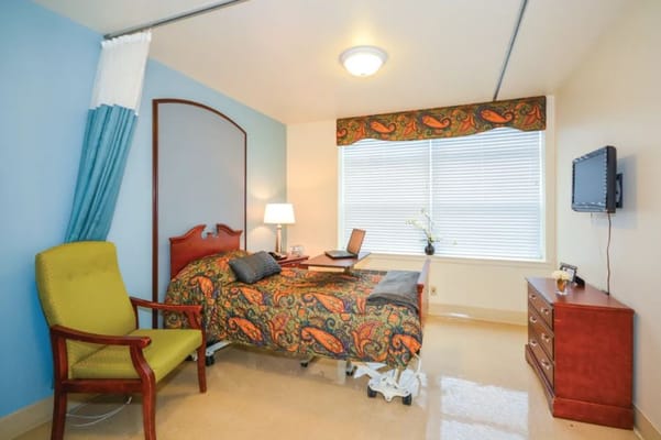 A cozy bedroom with a bed, chair, lamp, and window.