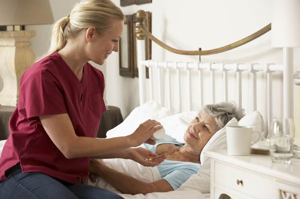 A nurse giving medication to a senior resident in bed.