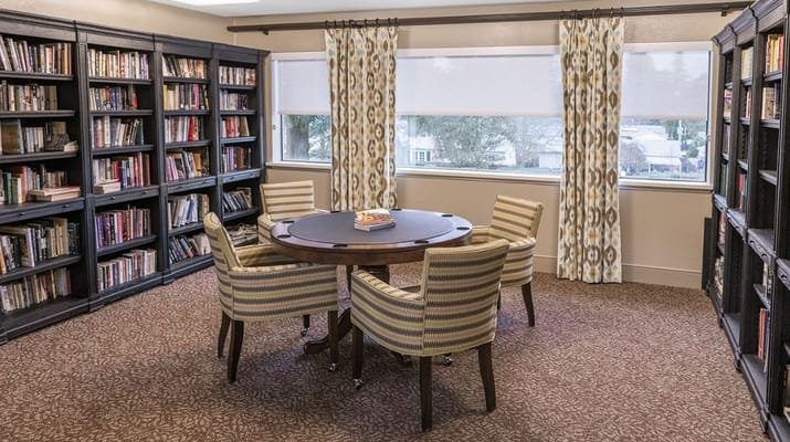 A library with bookshelves and a round table surrounded by chairs.