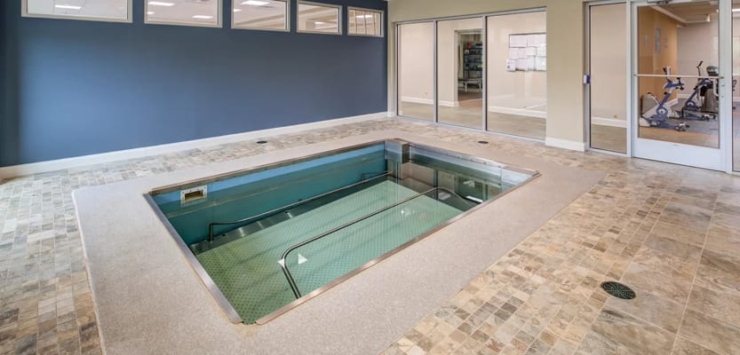 Indoor therapy pool with a tiled floor and large windows.
