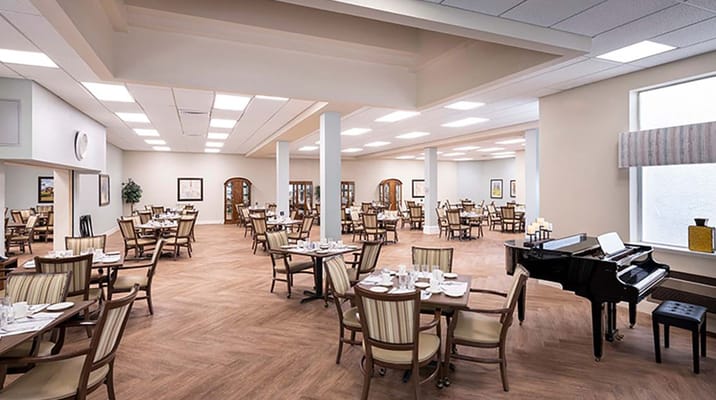 Spacious dining room with tables set for meals and a piano.