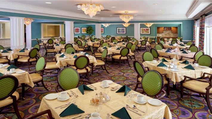 Spacious dining room with green chairs and tables set for meals.