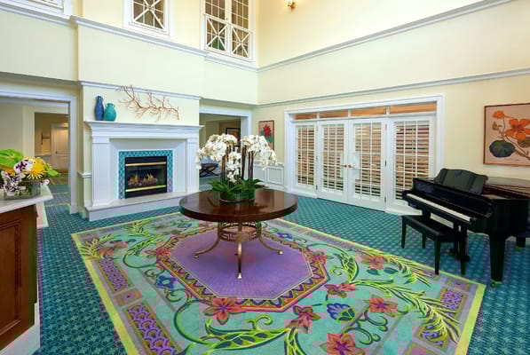 Bright and welcoming lobby with a floral rug, piano, and fireplace.