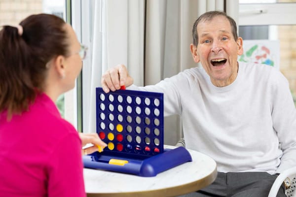 A resident playing a game with staff in a bright room